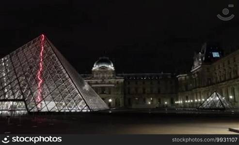 Hyperlapse shot of few people walking outside the Louvre and illuminated glass Pyramid at night. World famous art museum in Paris, France