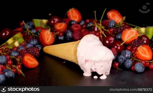 Ice cream with forest fruits background melting on black table.