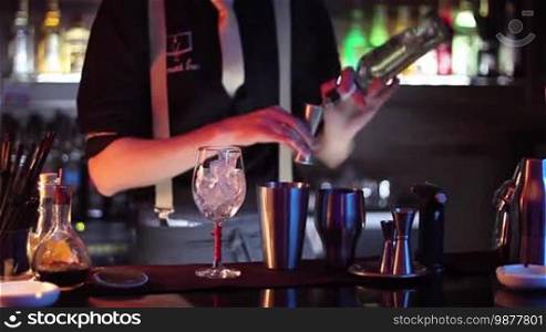 In a nightclub or pub, a professional bartender is preparing a cocktail with ice and a mix of alcohol. The bartender is measuring quantities for a perfect cocktail. Concept: disco, fun, friends, cocktail.