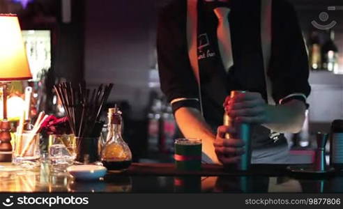 In a nightclub or pub, a professional bartender is preparing a cocktail with ice and a mix of alcohol. The bartender measures quantities for a perfect cocktail. Concept: disco, fun, friends, cocktail.
