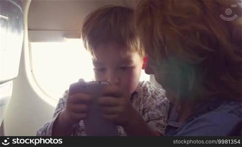 In the plane. Grandmother telling something to the grandchild while he is using a smartphone to entertain himself during the flight