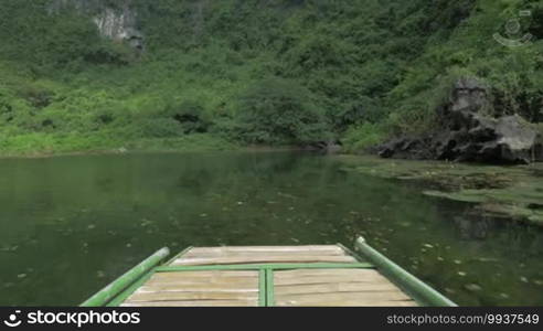 In Trang An Bai in Hanoi, Vietnam riding from first-person on boat on river with scenic views in a sunny day. Seen mountains, green trees and plants