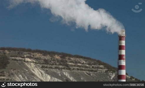 Industrial smokestack with billowing white smoke being pumped into the atmosphere against a blue sky