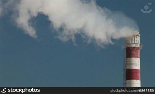 Industrial smokestack with billowing white smoke being pumped into the atmosphere against a blue sky