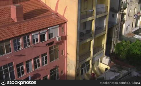 Innenhof / Hinterhof; adjacent tall apartment buildings; one in pink with a red tiled roof; one in yellow with balconies. The sun shines on the houses.