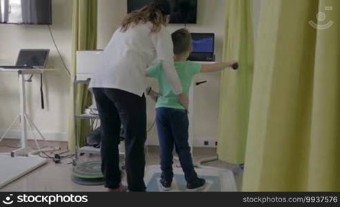 KALIKRATIA, GREECE - JANUARY 12, 2016: Rehabilitation Centre, Physiotherapy Clinic Evexia, female doctor examines small boy on the special equipment with laptop. Back side of view