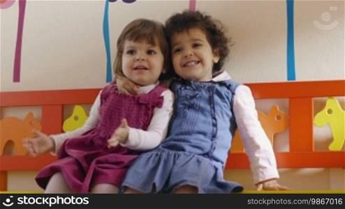 Kindergarten: Two cute baby girls play and hug in classroom
