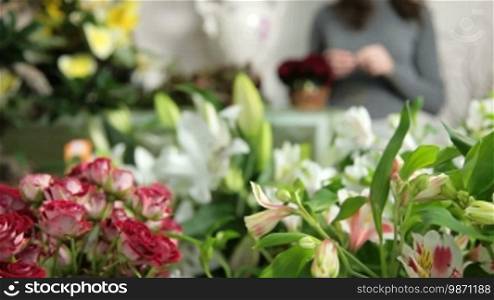 Large array of flowers in florist shop, in the background woman arranging Valentine's Day rose heart bouquet. Dolly shot