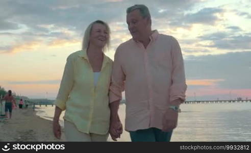 Leisure time on summer vacation. Senior couple having a relaxing evening walk along the seaside. Woman in the arms of a man