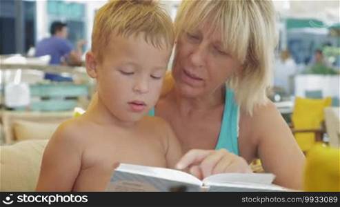 Little boy and grandmother spending leisure time with a book outdoors. They are looking at pictures and reading stories