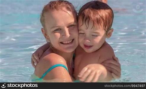 Little boy and his mother having fun in the swimming pool on bright sunny day