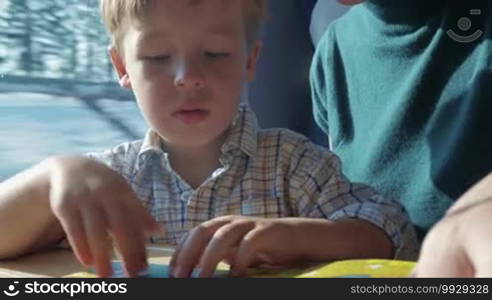 Little boy and mother reading children's book during ride in the train. Bright colorful pictures attract boy's attention