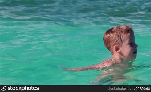 Little boy bathing alone in clear blue sea and talking to somebody