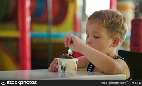 Little boy enjoying tasty chocolate ice cream in a cafe or game room