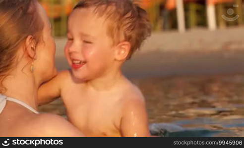 Little boy having fun at the seaside, laughing as his mother swings him up on her shoulder as they paddle together in the water