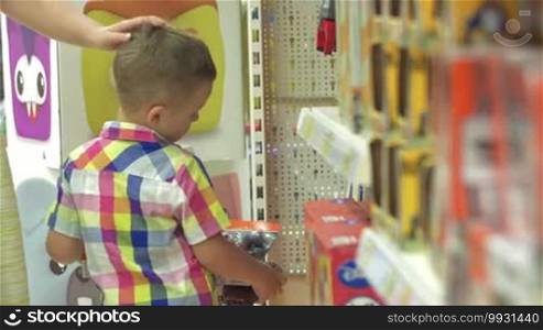 Little boy is standing in front of the shelf with toys and choosing the one.