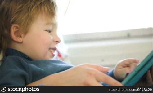 Little boy on mother's lap in the train using tablet PC held by mom