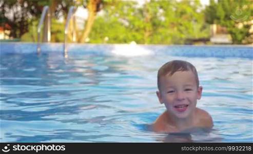 Little boy swimming alone in the outdoor pool. Funny kid enjoying summer vacation