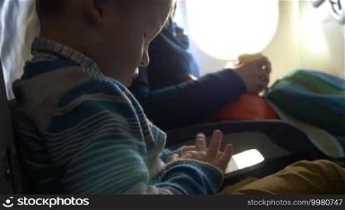 Little boy traveling by plane. He using smart phone to entertain himself during long and boring flight