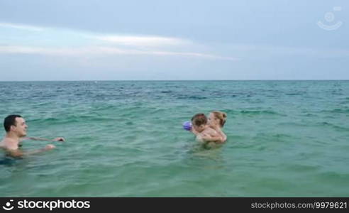 Little boy with ball making his own way in sea water walking from mother to father