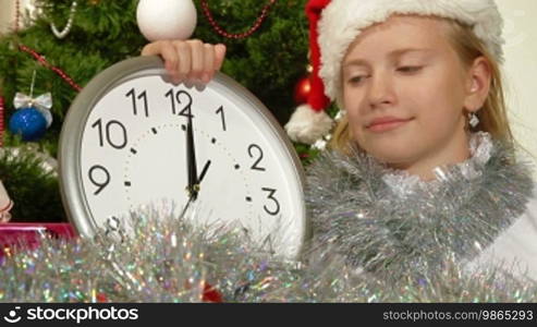 Little girl wearing Santa hat holding clock