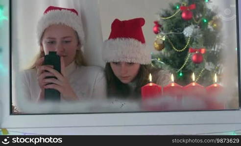 Little girls with gifted new smartphones at home near Christmas tree