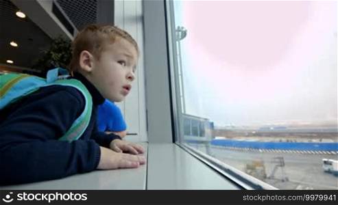 Little son and mother at the airport. They are looking out the window and pointing at something outdoors