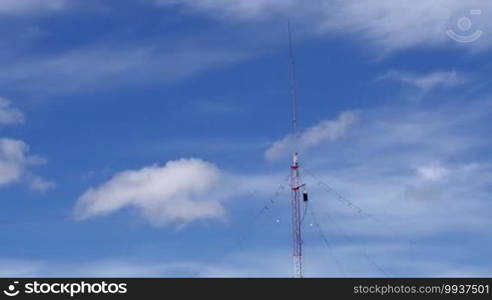 Long shot of a home-based single spike telecommunications antenna tower under light clouds during the day, with no birds in sight.