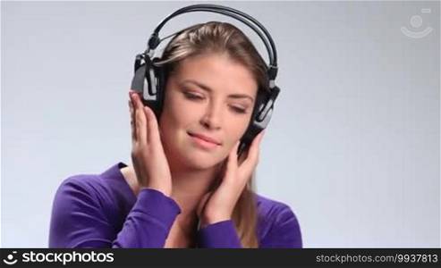 Lovely young woman with eyes closed relaxing listening to favorite song in headphones on the radio on white. Pretty brunette girl opening her eyes and confusedly smiling while enjoying music in earphones.
