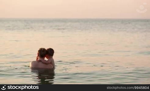 Loving mother and her young child bathing in the sea water by the beach in the sunset