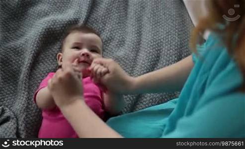 Loving mother doing gymnastics to laughing baby girl. Affectionate young mom massaging her lovely infant child. Top view. Shot over shoulder. Slow motion. Early development and health care concept.