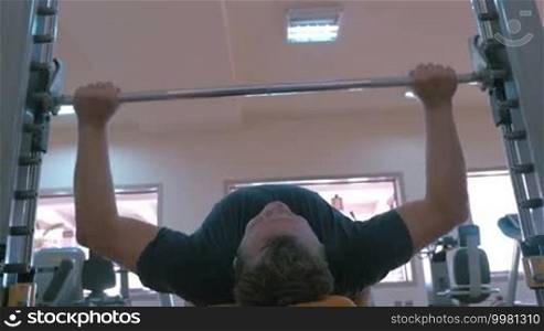 Low angle shot of a man doing strength exercise in a gym. Barbell bench press
