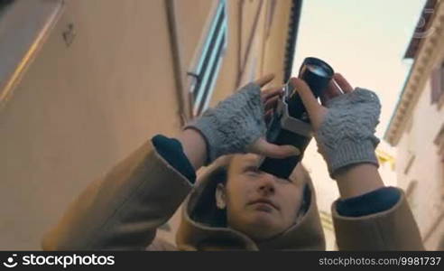 Low angle shot of a woman wrapped in making video of old European architecture. She walking in the street with retro camera