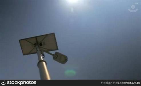 Low angle shot of street lamp getting electricity from the solar battery placed on the top. Blue sky and bright sunshine as background. Eco-friendly energy