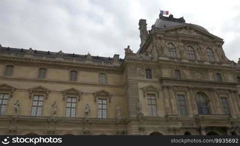 Low angle steadicam shot of moving along the Louvre, world's largest museum in Paris. French flag waving on the top