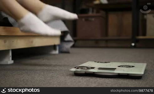 Low section of young woman in white socks standing on digital weight scale in domestic room. Closeup. Cheerful woman celebrating weight loss and joyfully jumping at home. Slow motion.