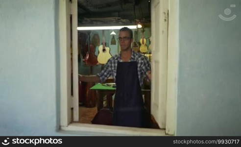 Lute maker shop and classical music instruments: young adult artisan opening his shop. He fixes an old classic guitar lacking a string. Dolly shot