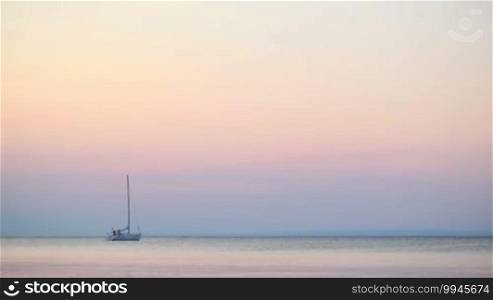 Luxury yacht moored offshore at sunset on a tranquil ocean under a delicate pink colored sky