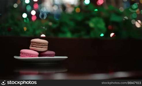 Macaroons on the table with focus on a female hand taking a picture of dessert using a phone camera.