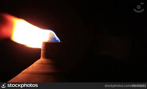 Macro shot of tiki torch flame at the seaside with copyspace from right.