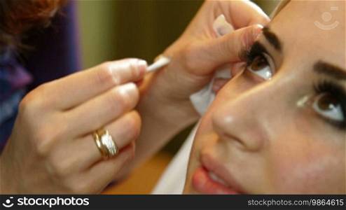 Makeup artist is using a brush to apply makeup to an attractive young woman's eyelids