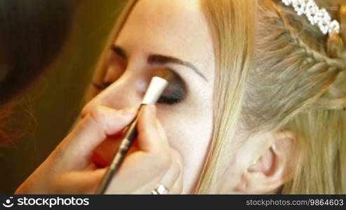 Makeup artist is using a brush to apply makeup to an attractive young bride