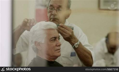 Male beauty, elderly barber cutting hair to customer in hair salon or men's beauty parlor