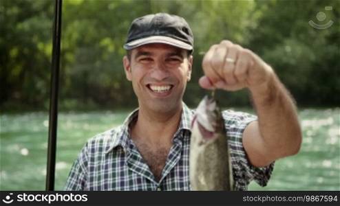 Man and sport, mid adult fisherman on holidays on river, relaxing and fishing trout, smiling and showing fish to the camera. Part 1 of 8