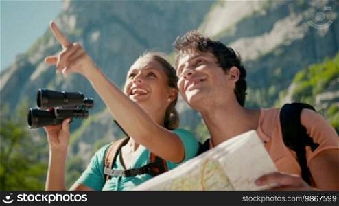 Man and woman during leisure activities on holidays, young people hiking and trekking on mountains, talking, and looking at map with binoculars. Part 3 of 12