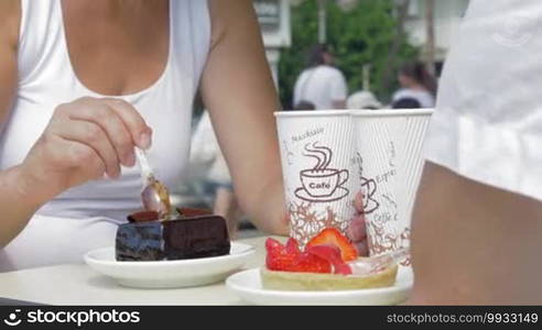 Man and woman eating chocolate and strawberry desserts and drinking coffee. Sweet toothers enjoying delicious cakes in outdoor cafe