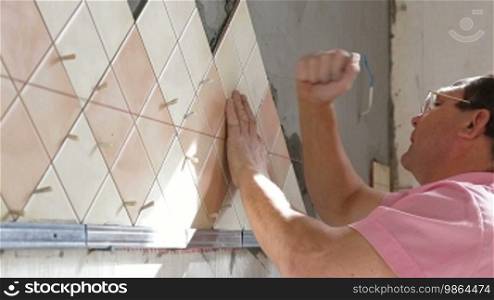 Man applying ceramic tile to a kitchen wall, side view, medium shot