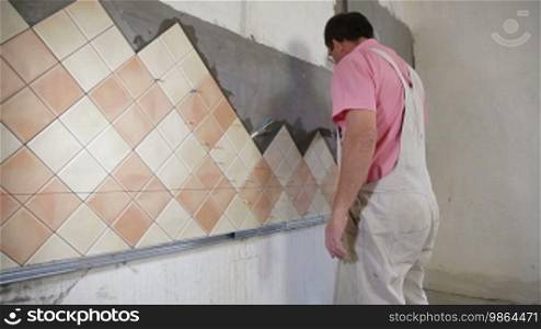 Man applying ceramic tile to a kitchen wall, working with a trowel