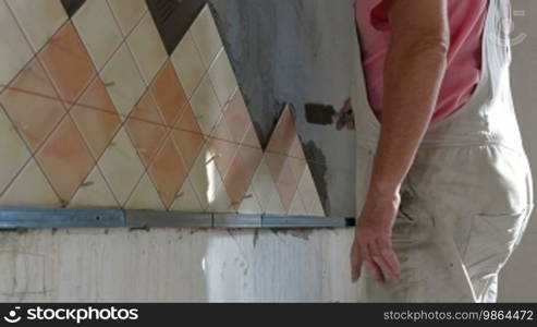 Man applying ceramic tile to a kitchen wall, working with a trowel, medium shot