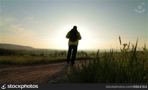 Man hiking through the morning field towards the sun